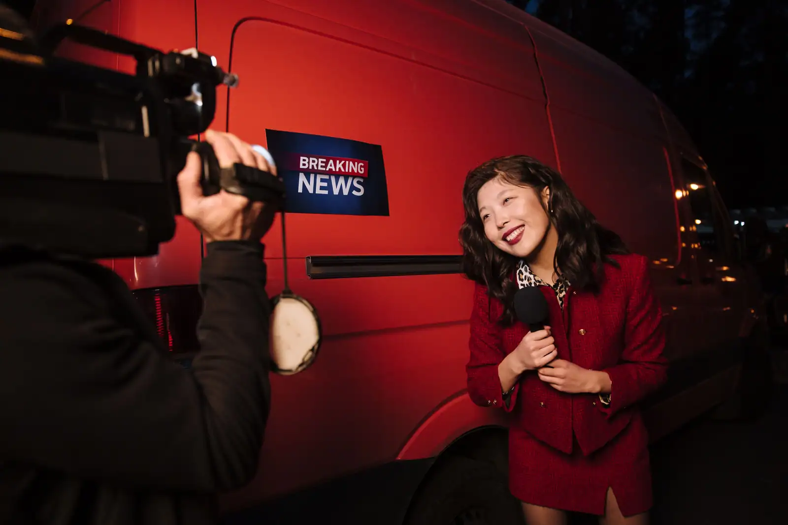 Journaliste au micro en reportage en direct devant un véhicule de presse, près d'un panneau Breaking News