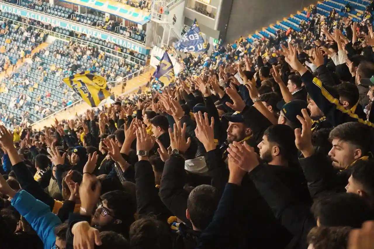 Supporters de football massés dans les tribunes d'un stade, encourageant leur équipe pendant un match