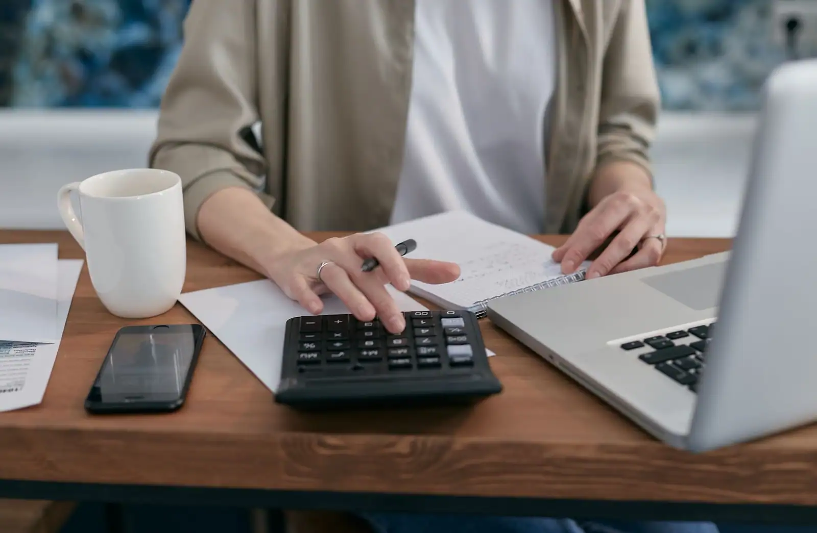 Mains utilisant une calculatrice et un ordinateur portable avec des documents sur un bureau en bois