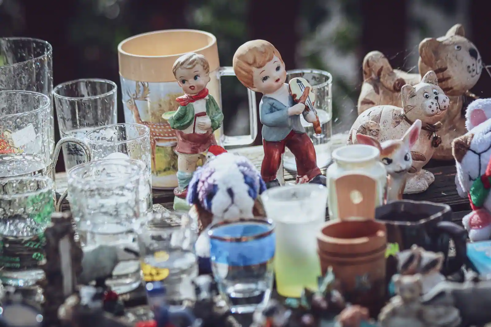 Objets d'occasion sur une table de brocante : figurines, peluches et verres anciens