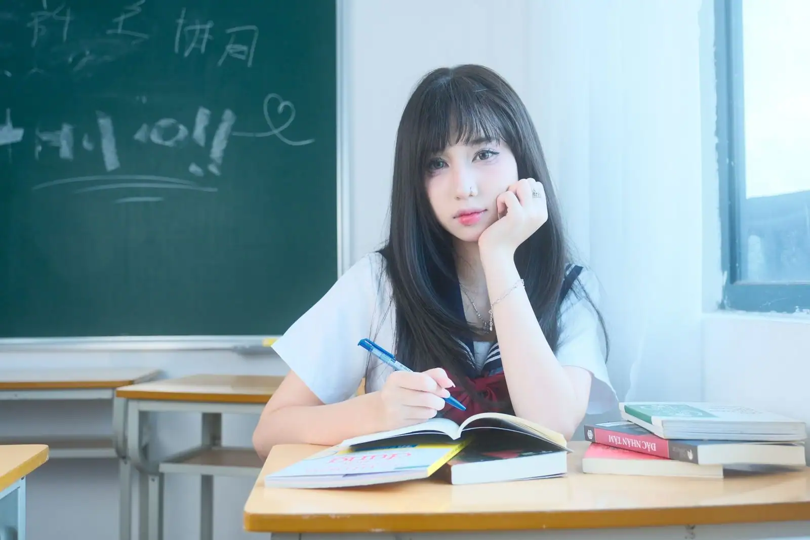 Élève en uniforme étudiant à un bureau de salle de classe, des livres ouverts devant elle