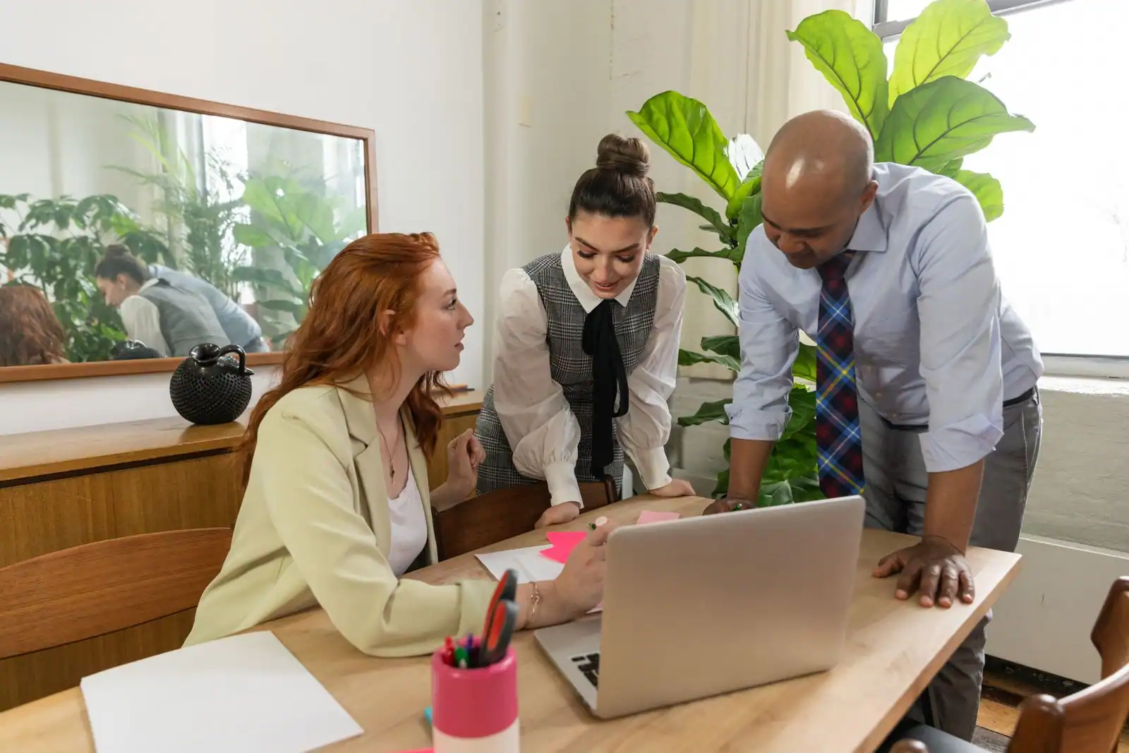 Trois collègues échangent autour d'un bureau avec un ordinateur portable, dans un espace de travail lumineux
