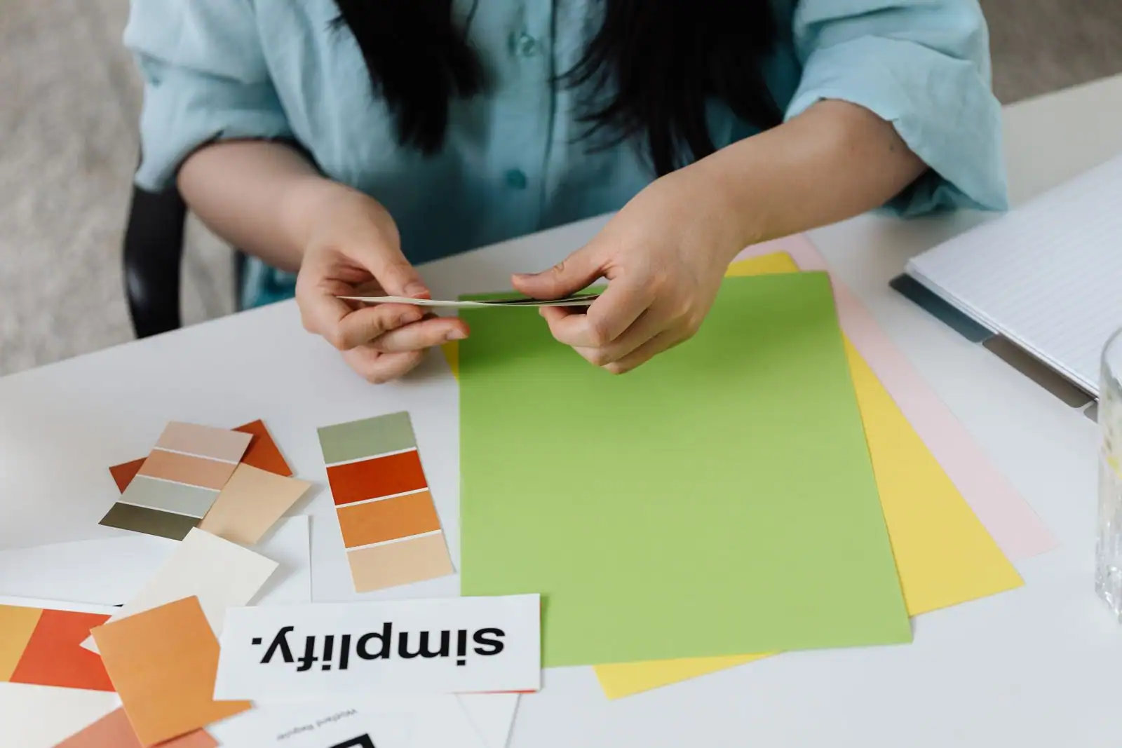 Personne comparant des nuanciers de couleurs et des échantillons de papier sur un plan de travail.