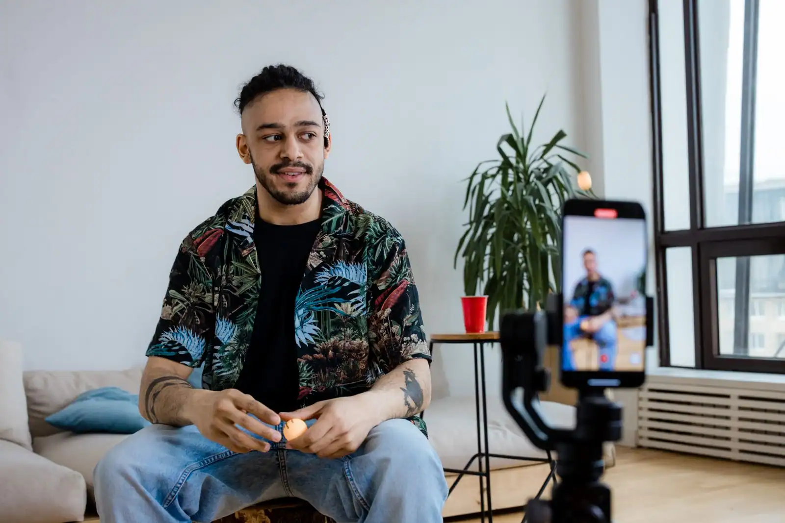 Personne enregistrant une vidéo face à un smartphone monté sur trépied, dans un salon