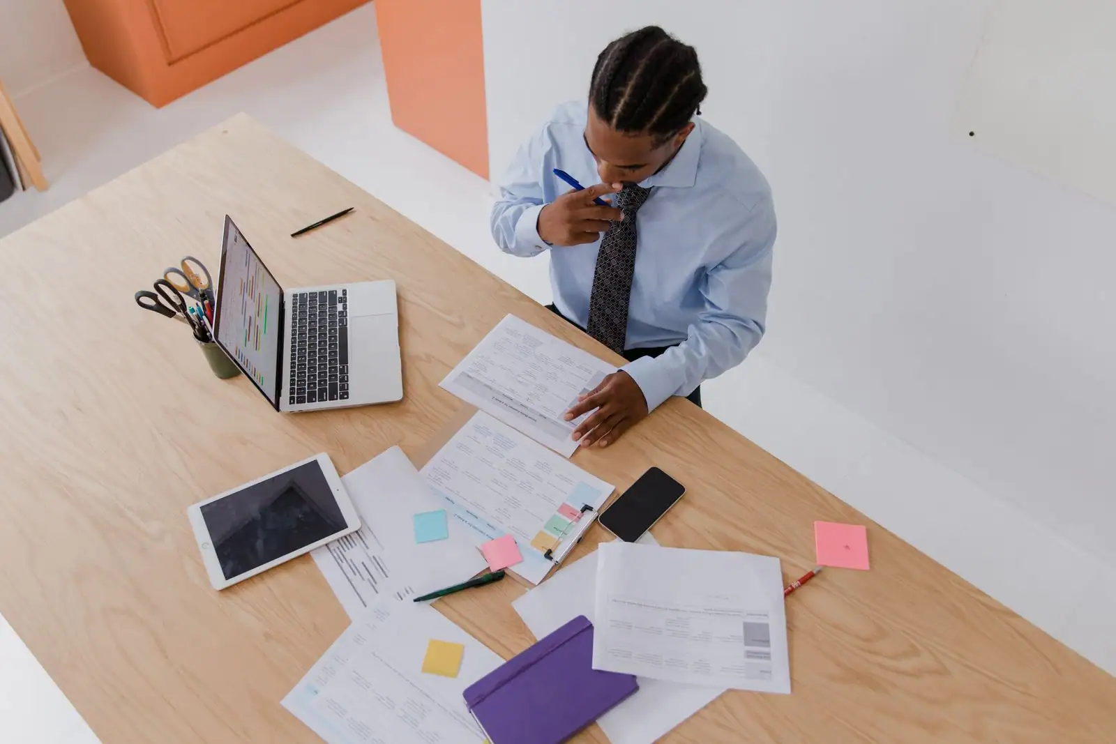 Homme en chemise concentré sur des documents de travail à un bureau, ordinateur portable ouvert