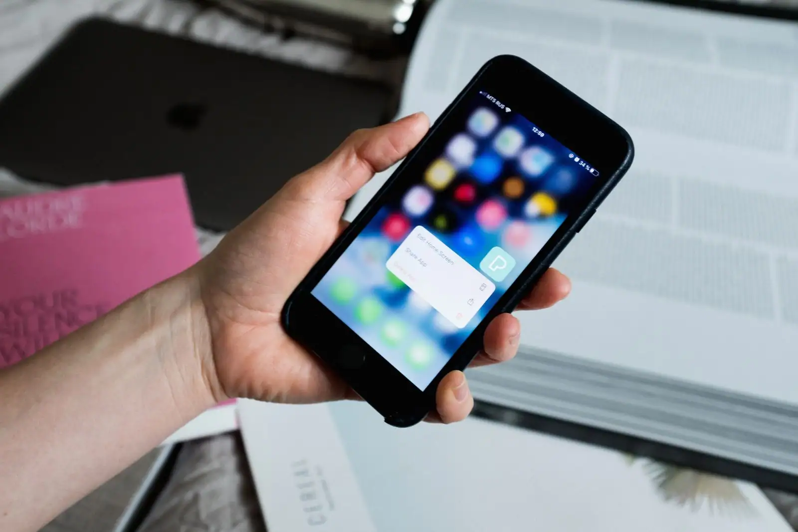 Main tenant un smartphone affichant des icônes d'applications, près de livres et d'un ordinateur portable