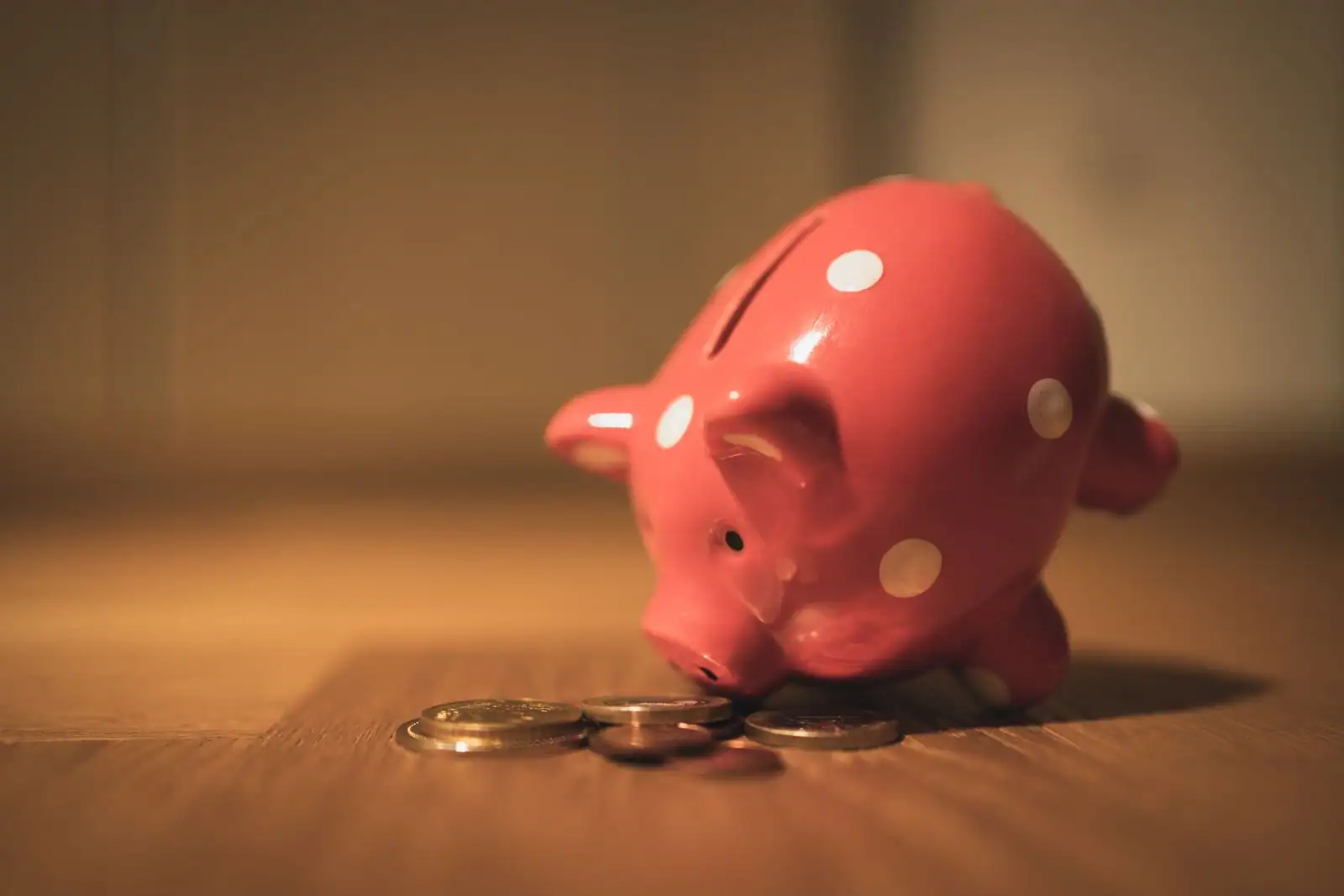 Tirelire à pois et quelques pièces de monnaie posées sur une surface en bois, symbole de l'épargne