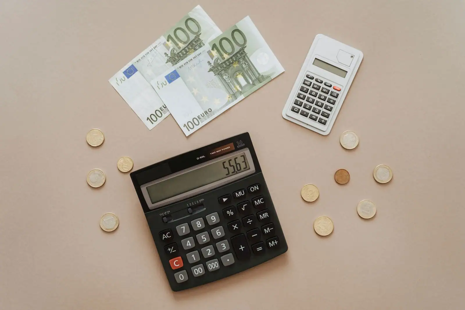 Billets de cent euros, pièces de monnaie et calculatrices posés sur une table, évoquant la gestion d'un budget