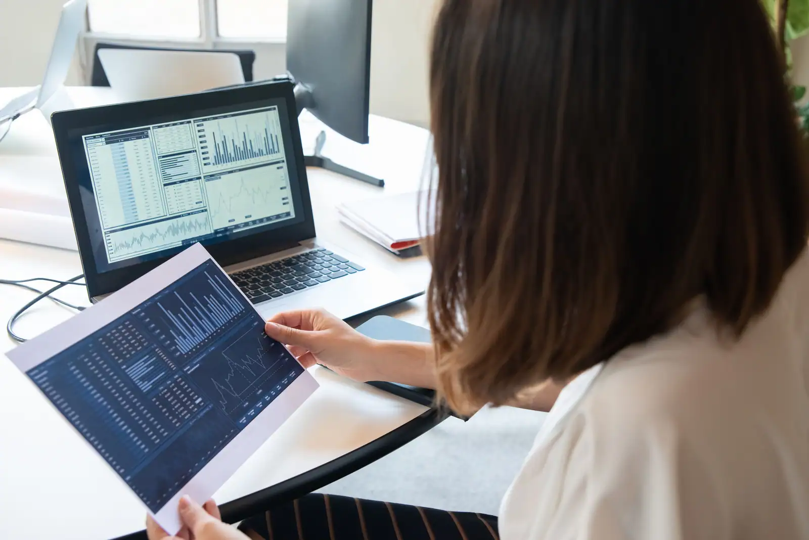 Une salariée examine des documents financiers chiffrés devant un ordinateur portable, à son bureau.