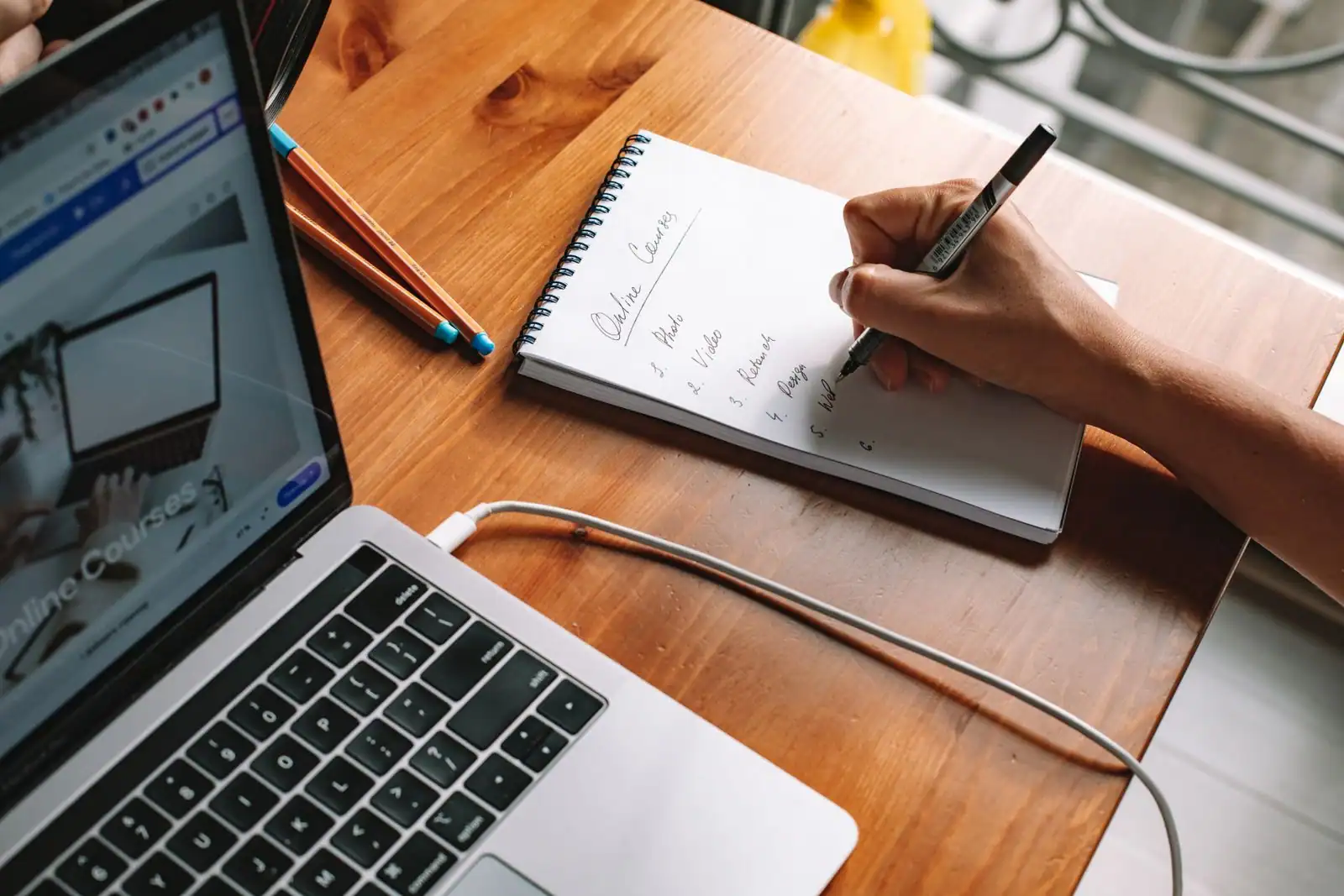 Main prenant des notes dans un carnet à côté d'un ordinateur portable affichant une plateforme de cours en ligne