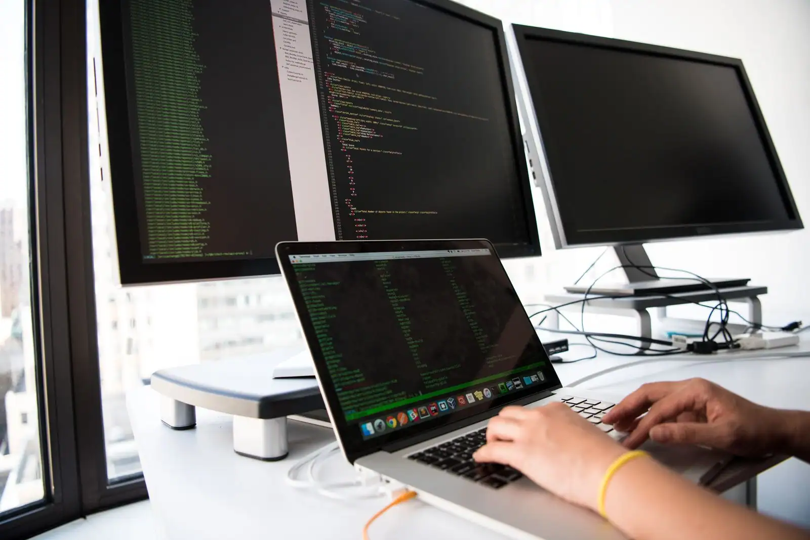 Développeur tech au travail sur son ordinateur, lignes de code affichées à l'écran dans un espace de travail.