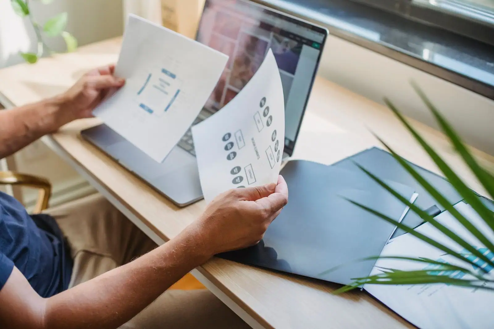 Personne examinant des maquettes de pages web imprimées devant un ordinateur portable