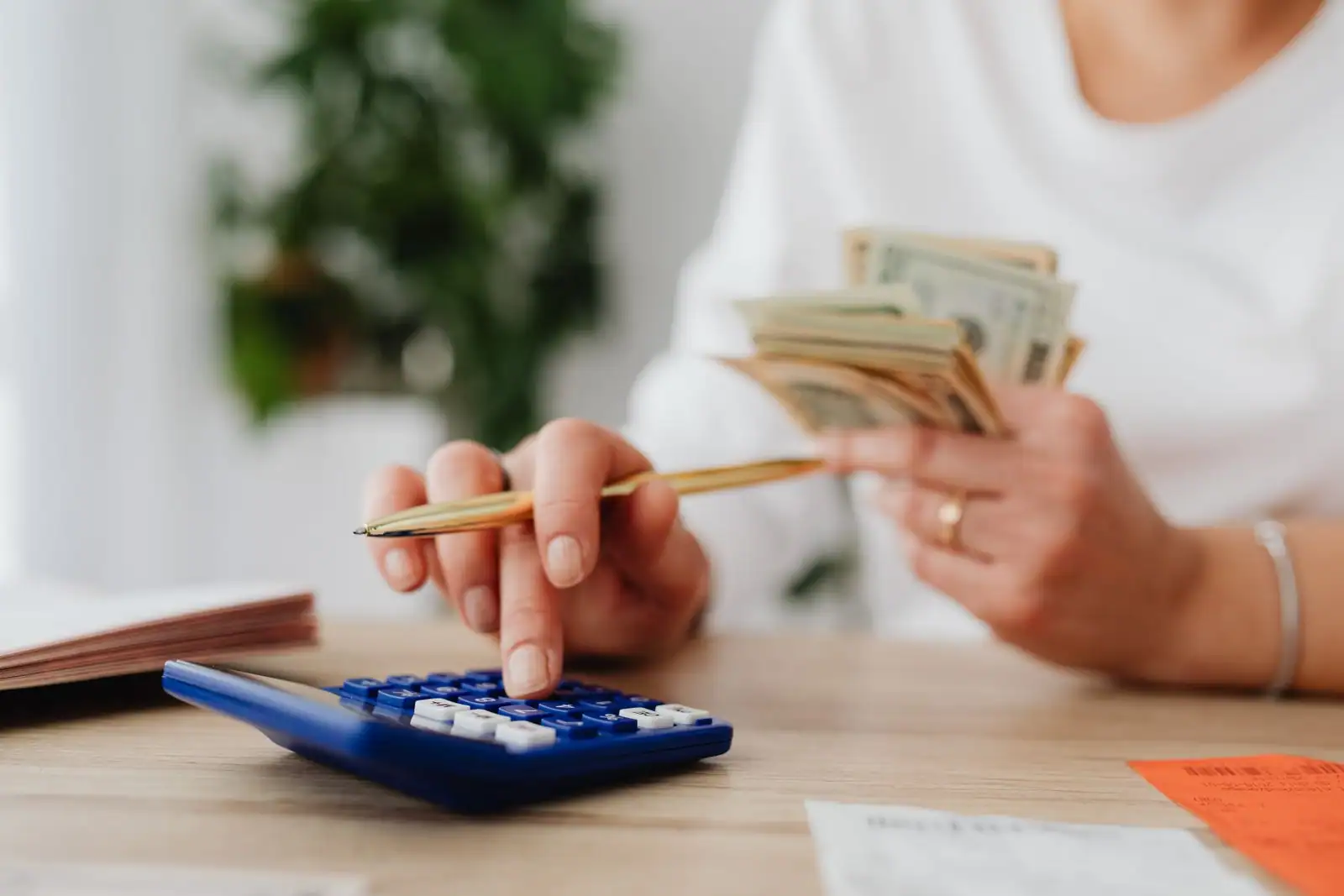 Personne fait ses comptes avec une calculatrice et des billets, un stylo à la main, sur un bureau