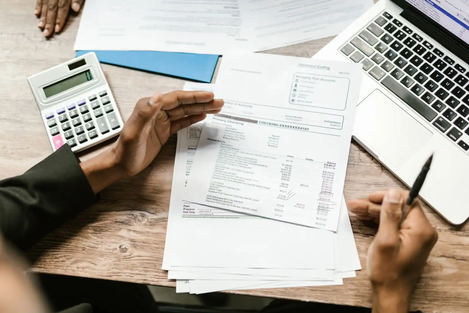 Personne examine des relevés bancaires avec une calculatrice et un stylo sur un bureau