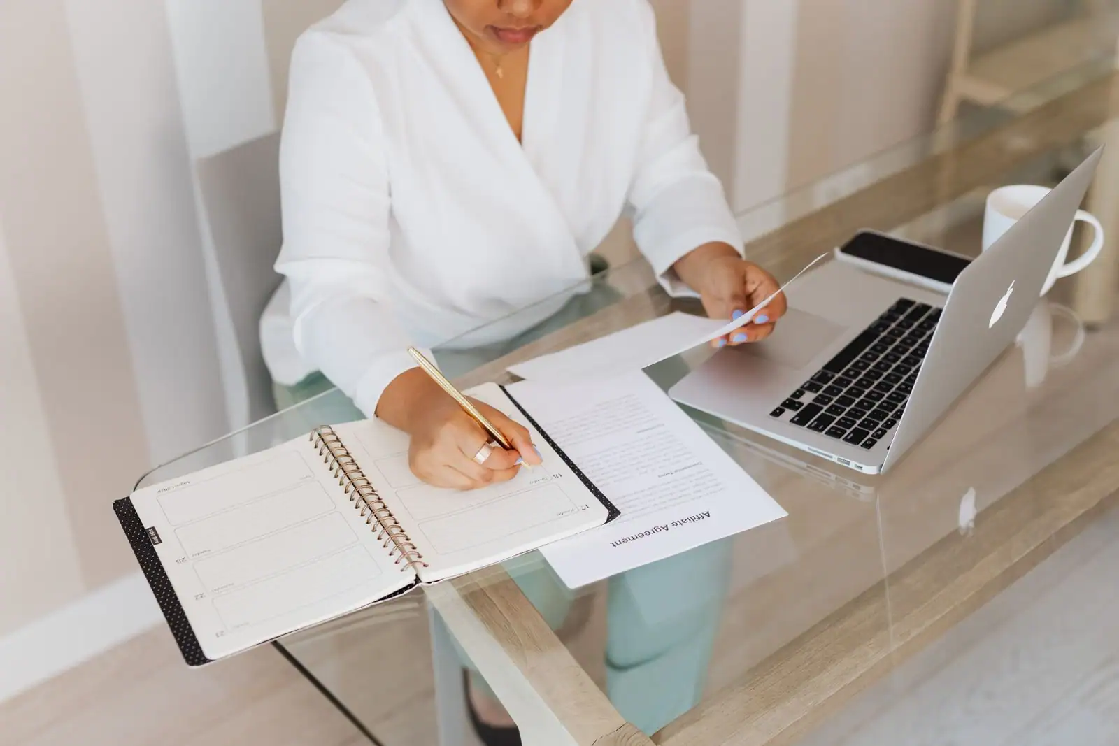 Personne en blazer clair écrivant dans un agenda à son bureau, à côté d'un ordinateur portable