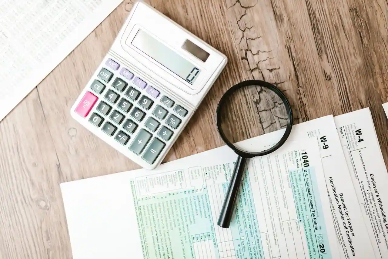 Une calculatrice et une loupe posées sur une déclaration de revenus, illustrant le calcul de l'impôt.