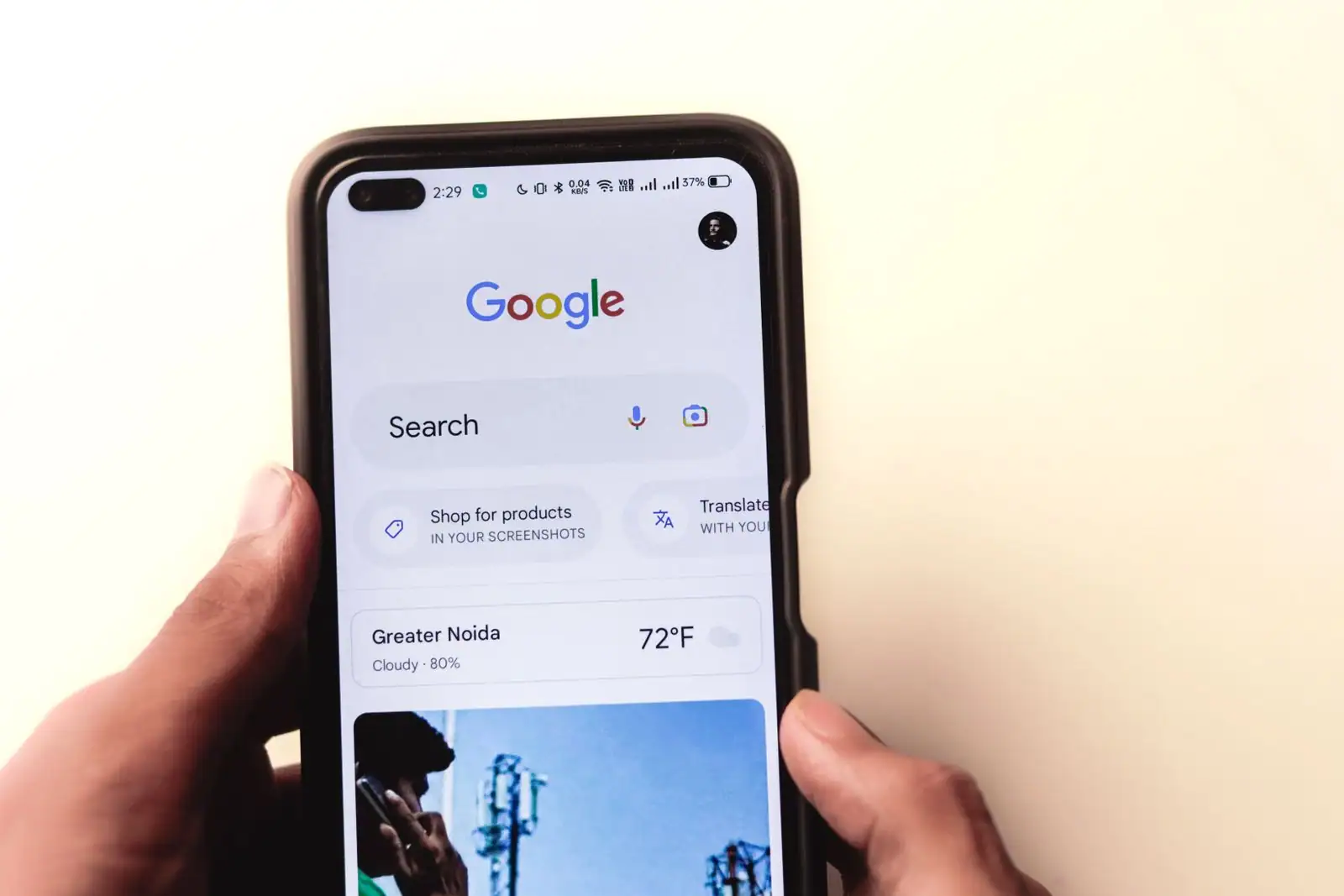 Mains tenant un smartphone affichant la barre de recherche Google sur fond clair