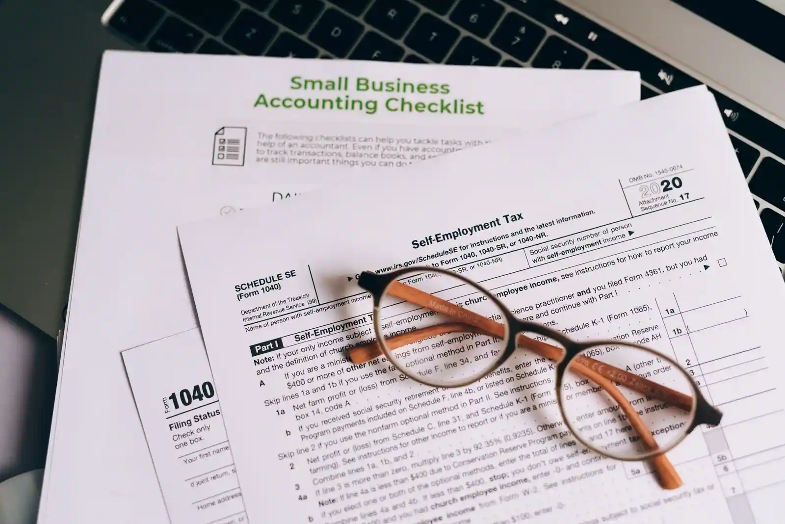Documents comptables et lunettes posés sur un ordinateur portable, illustrant la gestion d'une activité indépendante.