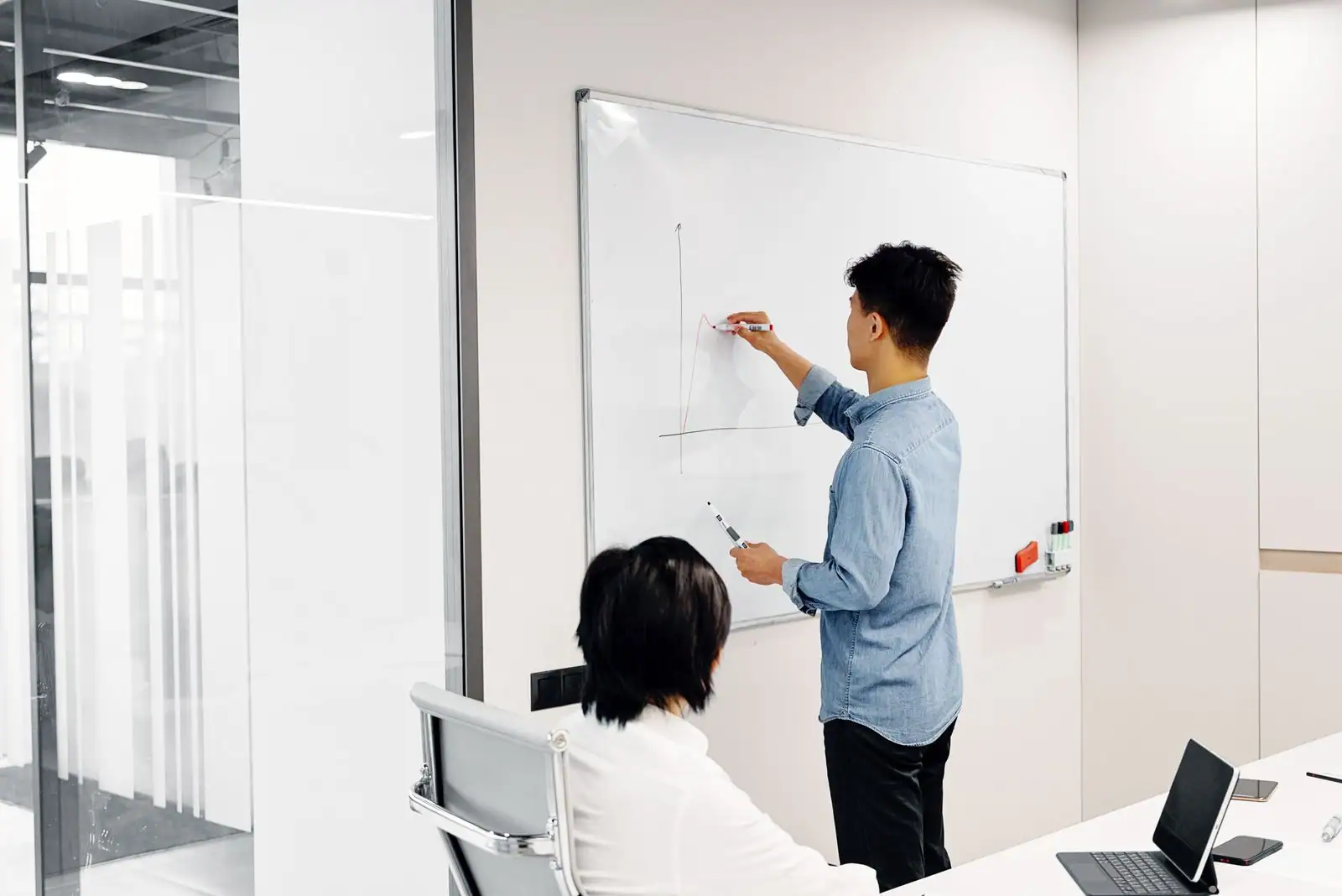 Personne dessinant un schéma sur un tableau blanc lors d'une réunion de travail