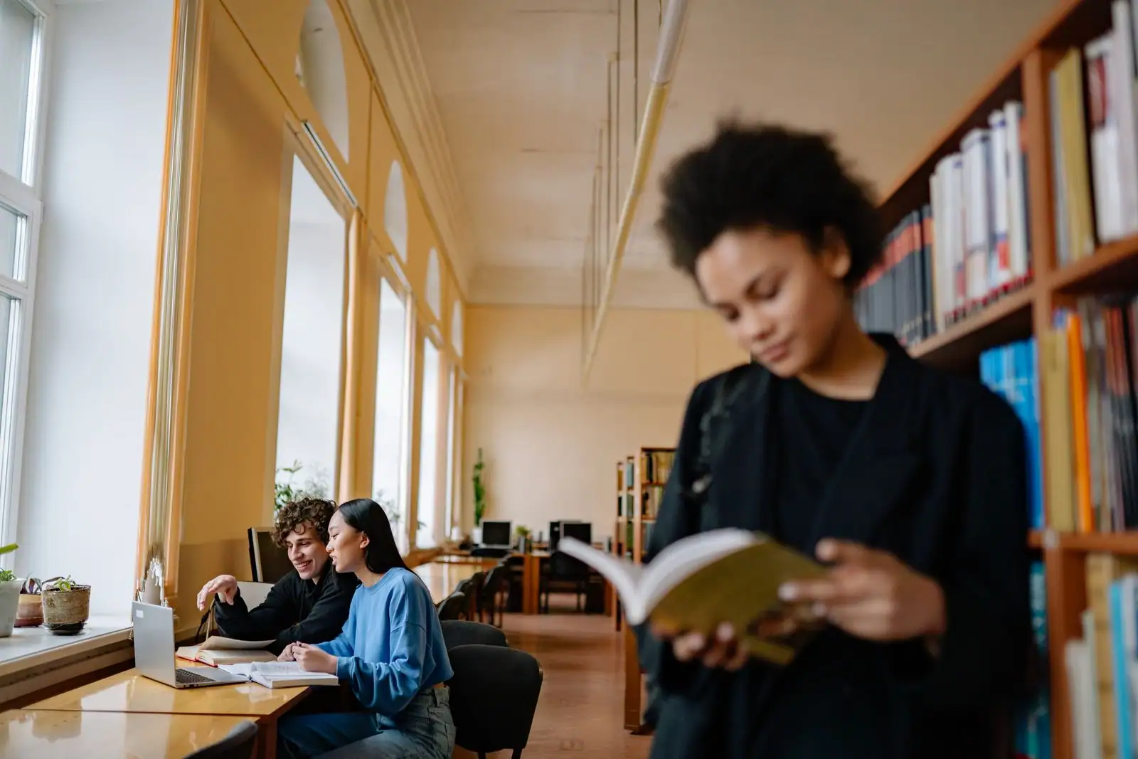 Une étudiante travaille sur son ordinateur portable au milieu de livres, dans une bibliothèque universitaire.