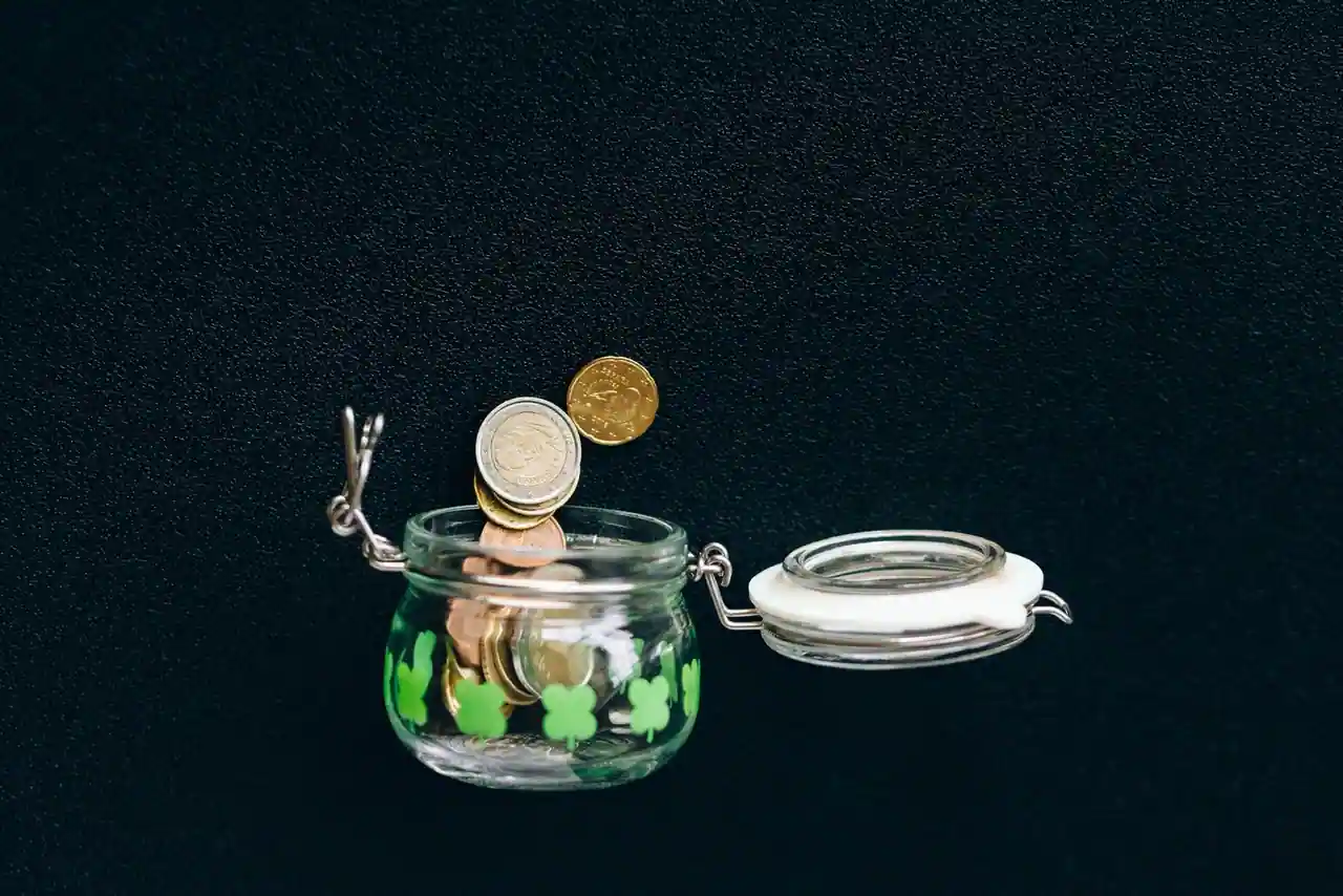Des pièces de monnaie déposées dans un bocal illustrent une épargne mise de côté progressivement.
