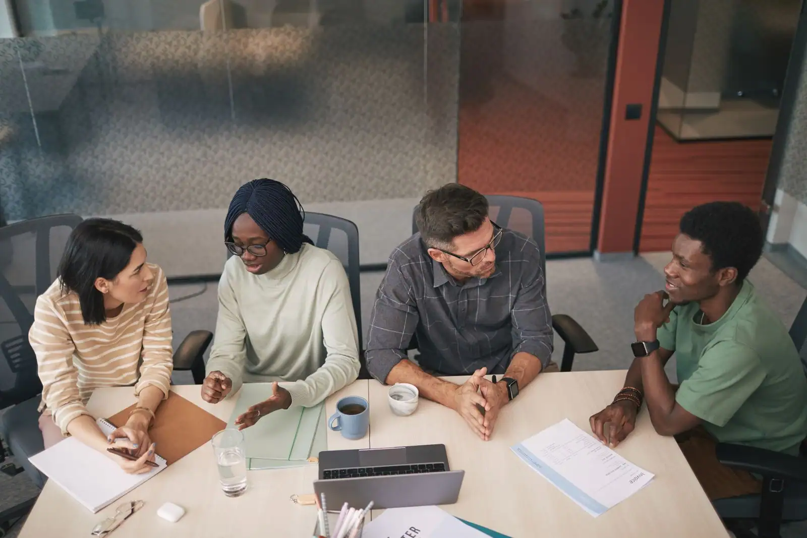 Une équipe échange autour d'une table de réunion, chacun participant à la discussion dans un bureau clair.