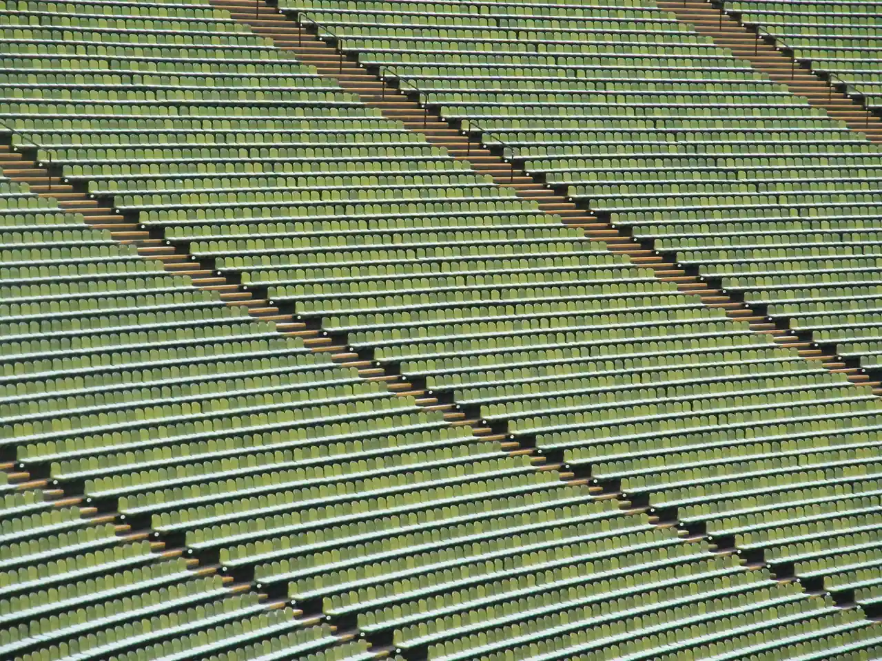 Rangées de sièges verts vides dans les tribunes d’un stade, vues depuis le haut des gradins