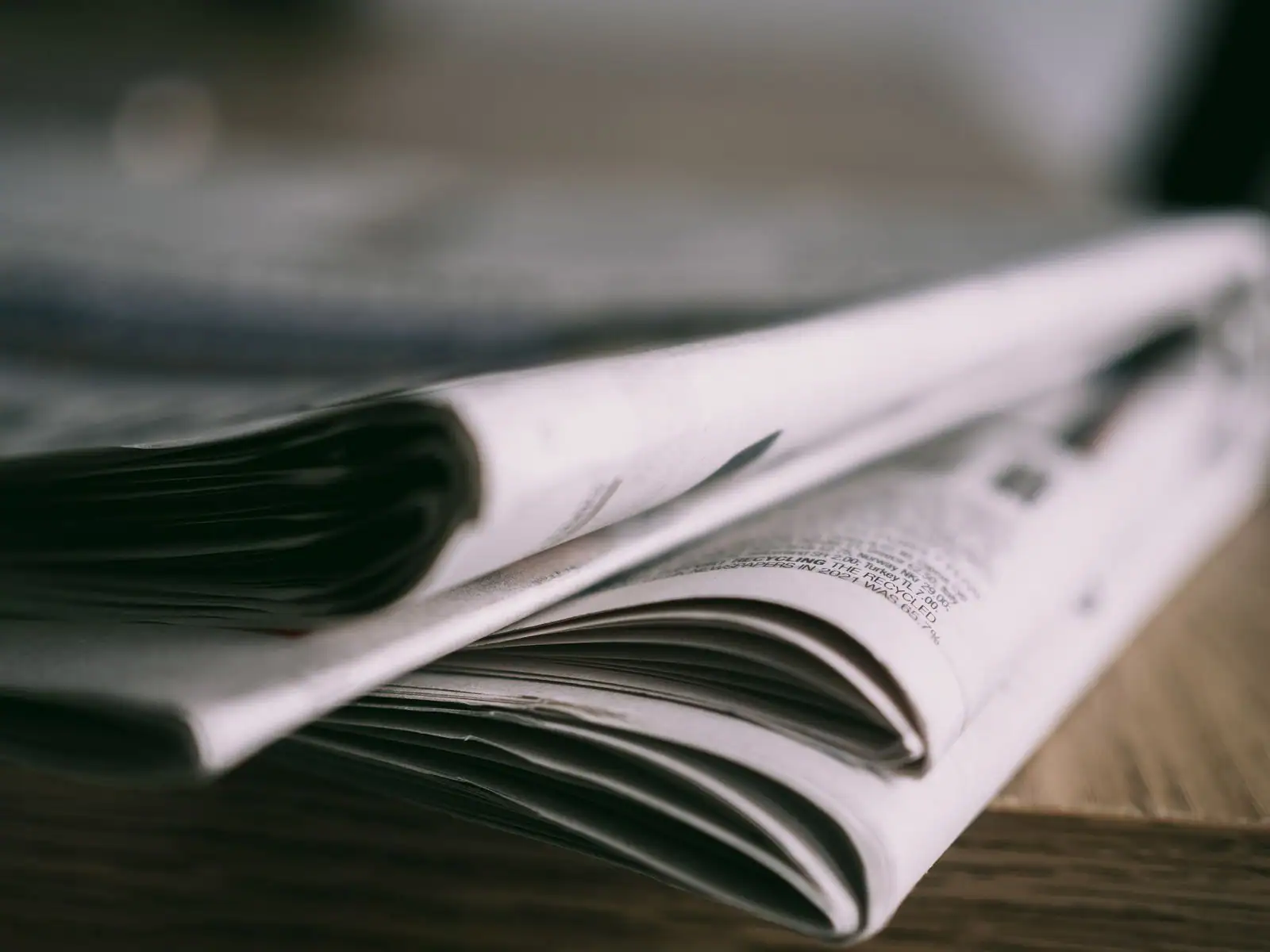 Journaux imprimés pliés et empilés sur une table en bois, pages ouvertes en gros plan.