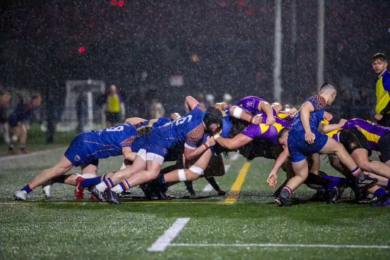 Mêlée de rugby engagée sous une pluie battante, lors d'une rencontre disputée en nocturne.