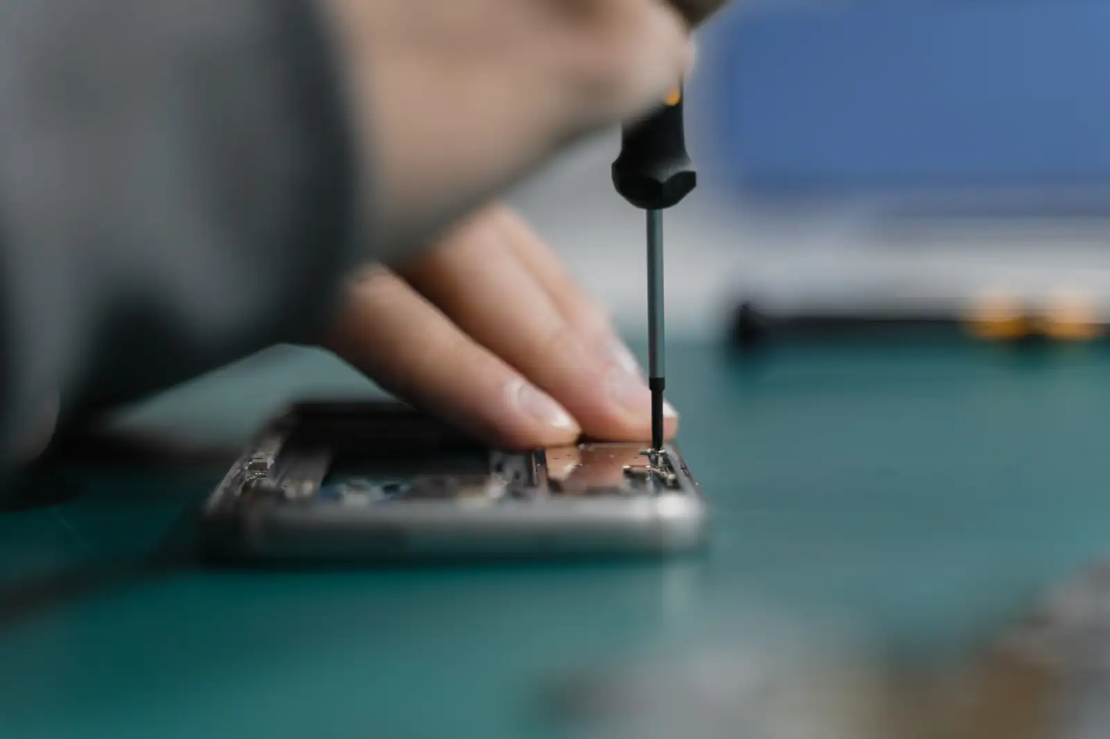 Main d’un réparateur maniant un tournevis de précision sur un smartphone ouvert, posé sur un tapis