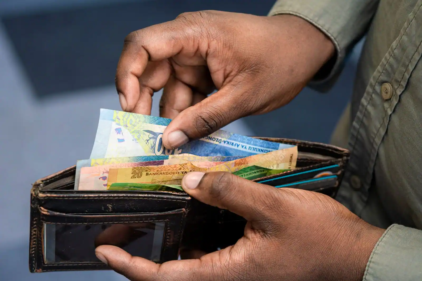Gros plan sur des mains sortant des billets en rands sud-africains d’un portefeuille en cuir.