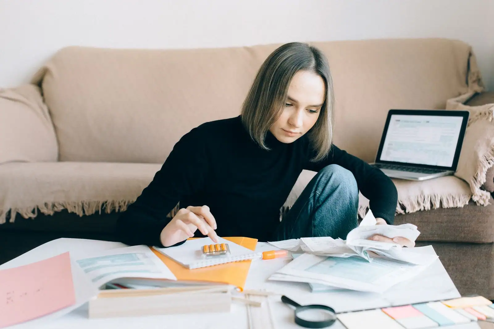 Femme assise devant une table basse couverte de formulaires et de justificatifs, ordinateur portable ouvert