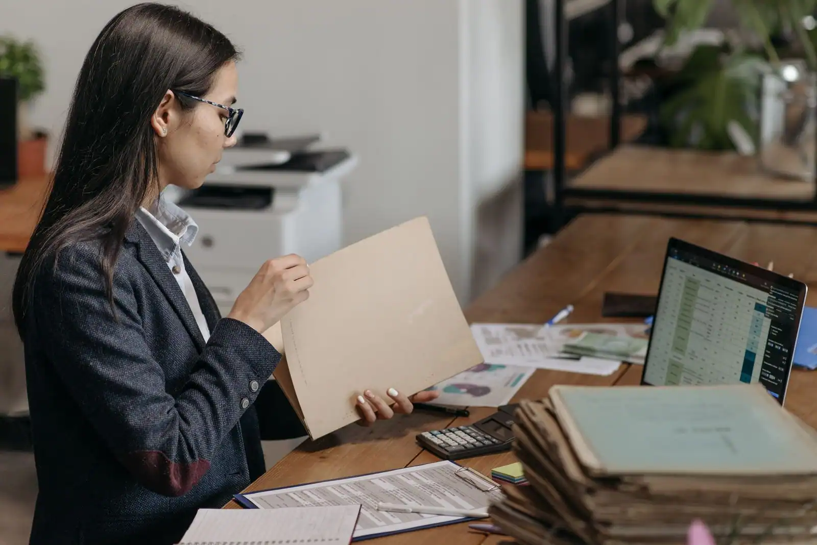 Professionnelle examinant un dossier cartonné à son bureau, ordinateur portable et piles de dossiers