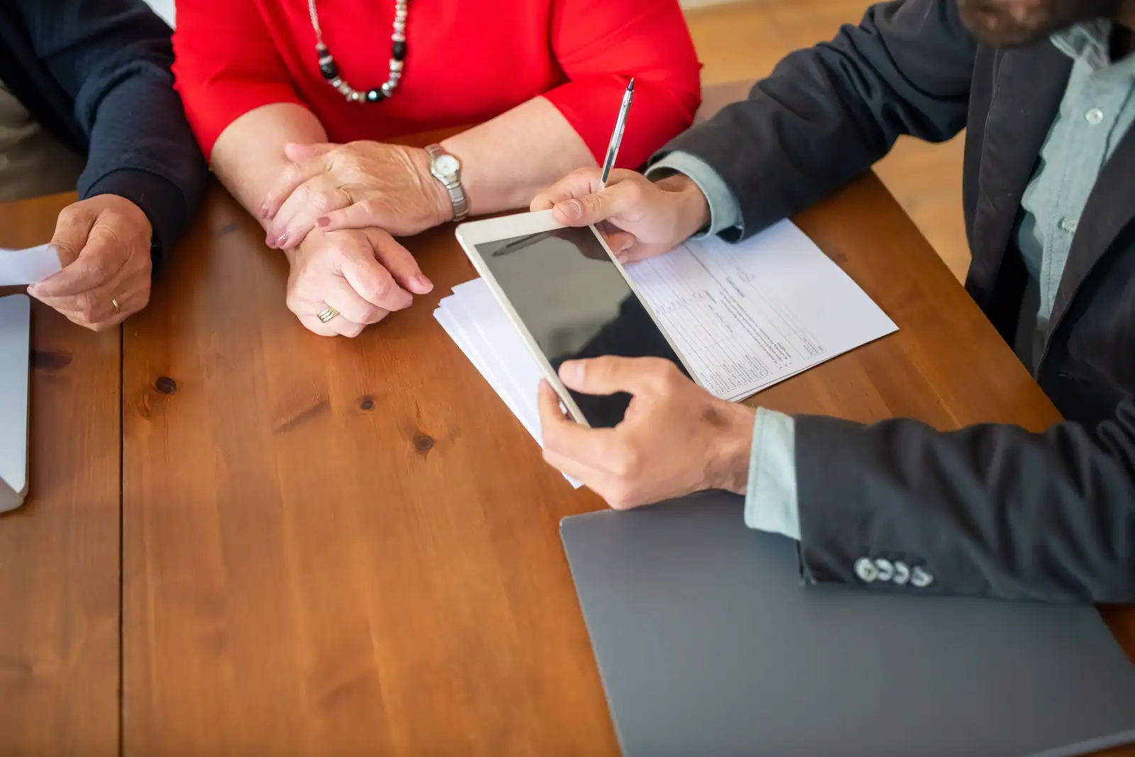 Un conseiller tient une tablette et un stylo au-dessus d'un document, face à un couple assis à une table en bois.