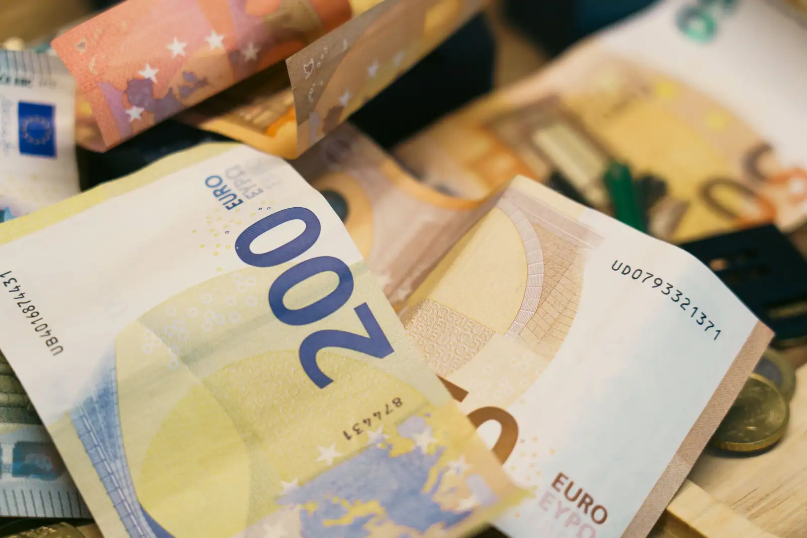 Billets en euros de 50 et 200 empilés en désordre, avec quelques pièces, sur un plan en bois.