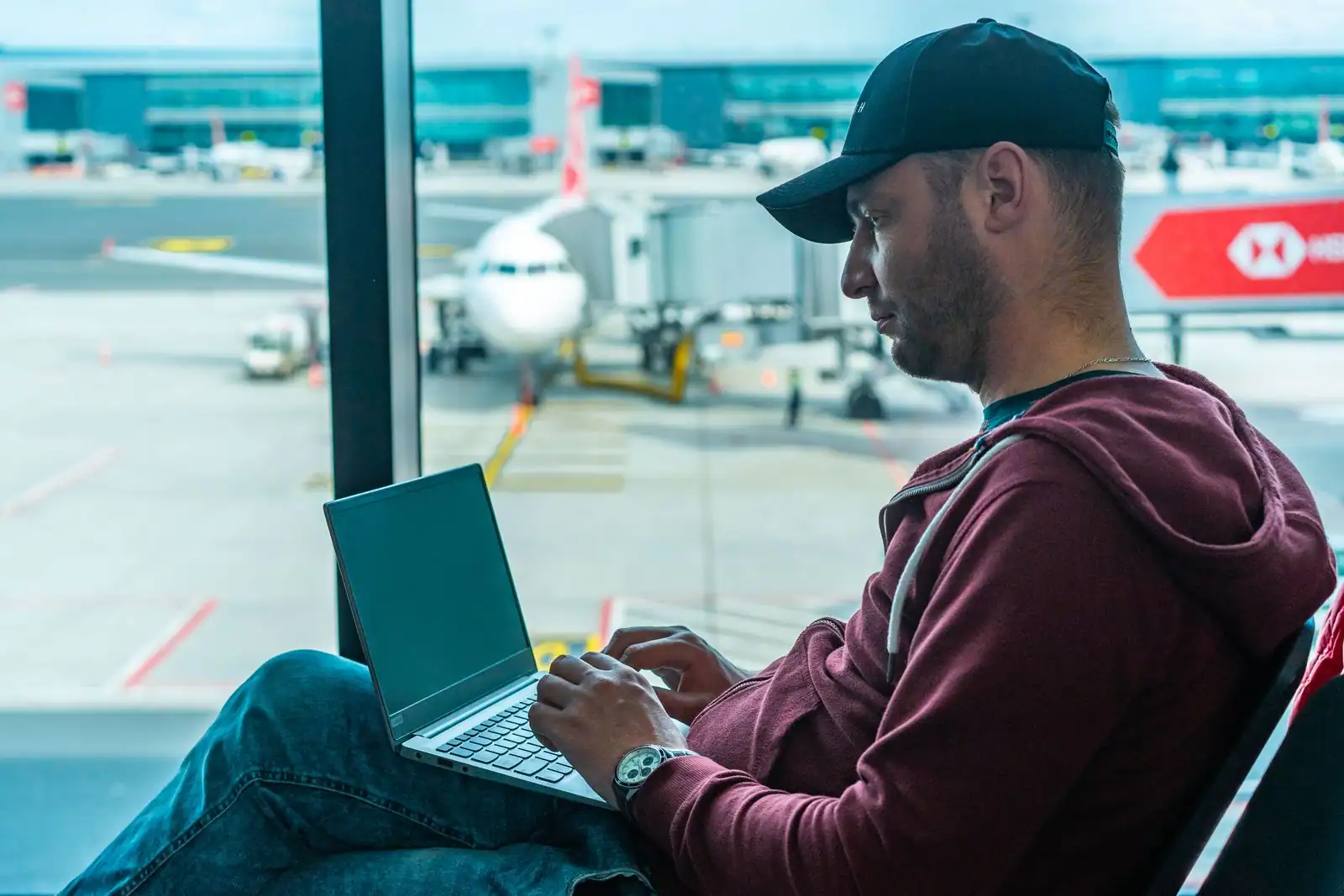 Voyageur travaillant sur son ordinateur portable dans une salle d'embarquement, avion visible derrière la vitre.