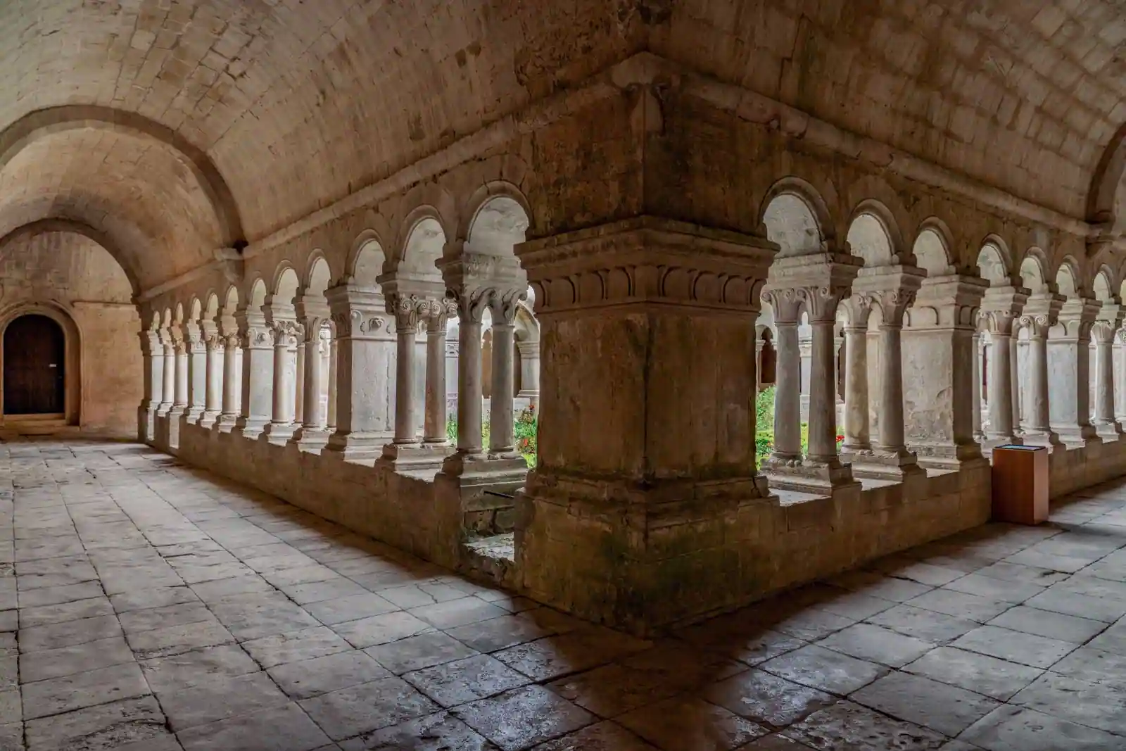 Galerie voûtée d'un cloître de monastère, arcades de pierre bordant une longue allée déserte.