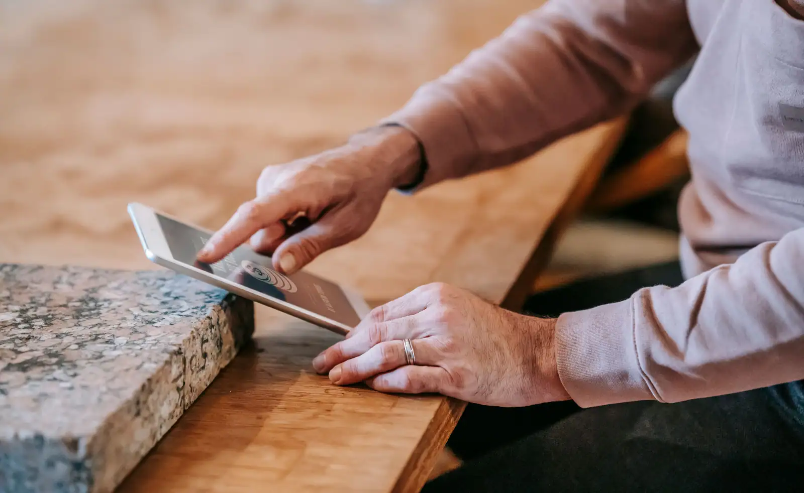 Une main fait défiler du bout du doigt le contenu affiché sur une tablette posée sur une table en bois